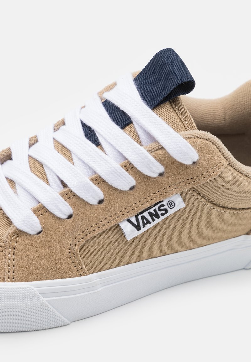 Beżowe sneakersy z płótna z białymi sznurówkami i granatowym akcentem. Posiadają gumową podeszwę, teksturowane panele boczne oraz metkę z logo po zewnętrznej stronie.