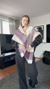 Rutet skjerf i mykt stoff, med nyanser av rosa, burgunder og grått. Kantene er frynset; båret drapert over et svart antrekk.