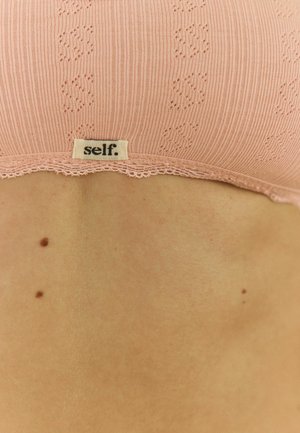 Pink ribbed bra with lace trim, featuring a subtle pattern and a label reading "self." Positioned against a backdrop of skin.