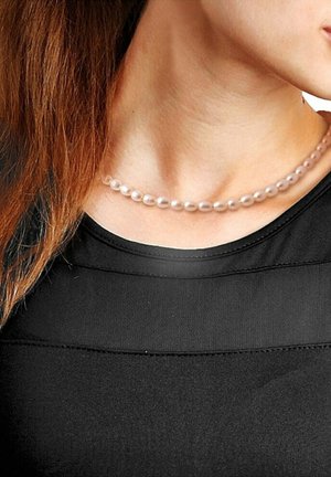 Collier en perles roses avec des perles ovales, présentant une finition lisse et brillante. Porté sur un haut noir, mettant en valeur son élégance subtile.