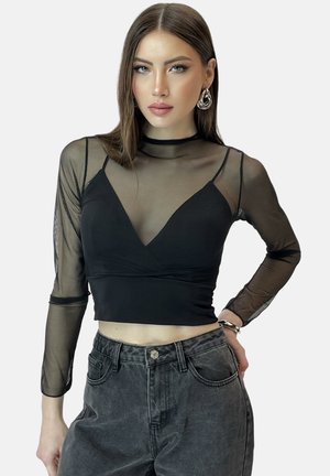 Top corto nero a maniche lunghe con accenti in rete trasparente, scollatura rotonda e corsetto aderente. Abbinato a jeans grigi a vita alta.