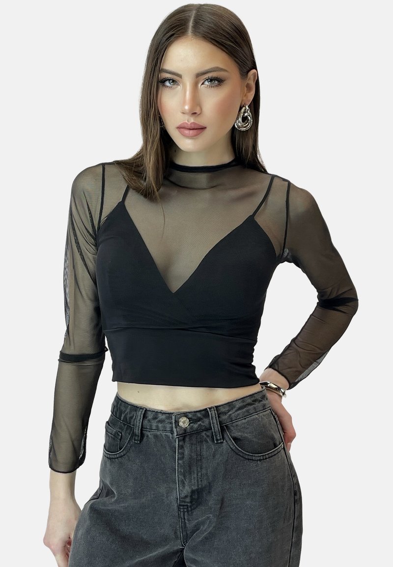 Schwarzes langärmliges, cropped Oberteil mit durchsichtigen Mesh-Akzenten, Rundhalsausschnitt und tailliertem Schnitt. Kombiniert mit grauen, hoch taillierten Jeans.