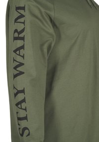 Maglietta a maniche lunghe verde oliva con testo nero in grassetto "STAY WARM" lungo la manica sinistra. Tessuto di cotone morbido. Cappuccio con cordoncino regolabile.