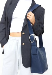 Borsa a secchiello in pelle blu navy con una larghezza della tracolla e dettagli in metallo argentato. Texture liscia, silhouette strutturata.