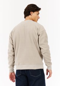 Lichtbeige fleecetrui met een ronde halslijn, ribgebreide manchetten en onderrand. De stof heeft een zachte, gestructureerde afwerking. Draag met donkere jeans.
