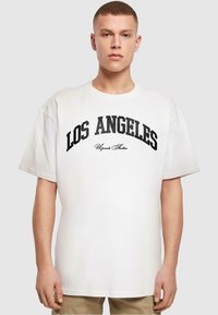 Hvid bomulds t-shirt med fed sort tekst "LOS ANGELES" buet henover brystet, med korte ærmer og lige kant.