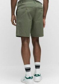 Olivgröna shorts med rak passform; har bakfickor med knappar och sidofickor; bärs med vita strumpor och skor med gröna detaljer.