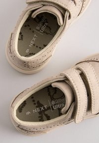 Beige suede shoes with two Velcro straps, perforated detailing, and patterned insoles featuring "NEXT Ortholite Ultra" branding.