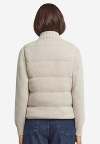 Beige stickad väst med hög krage, försedd med en vadderad puffer-bak. Ribbade ärmar och nederkant med en subtil textur.