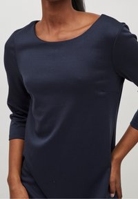 Robe en tissu lisse bleu marine avec un col arrondi et des manches trois-quarts, présentant des lignes simples et épurées ainsi qu'une coupe décontractée.