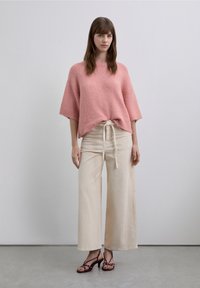 Pull rose texturé à coupe décontractée et manches courtes, associé à un pantalon crème à jambes larges côtelé et des sandales à talons bordeaux.