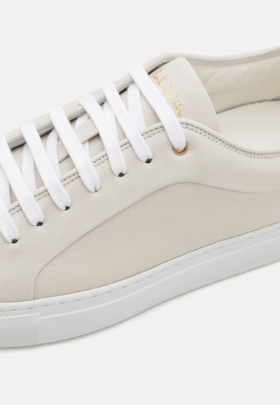 White leather sneaker with flat white laces, gold branding detail on the tongue, and a textured rubber sole. Features sleek, minimalist design.
