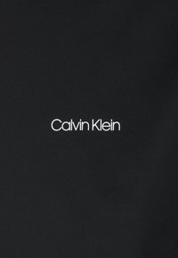 Tessuto nero con il testo bianco "Calvin Klein" in un carattere sans-serif moderno, centrato e chiaramente leggibile sullo sfondo.