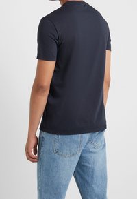 Mörkblå t-shirt med kort ärm i bomull. Rund halsringning och mjukt material, kombinerad med ljusblå jeans och synliga sömmar.