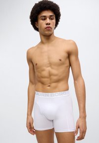 Λευκά ανδρικά μπόξερ με γκρι ζώνη μέσης «BJÖRN BORG», βαμβακερό υλικό, εφαρμοστή γραμμή και ραμμένα λεπτομέρειες. Το μοντέλο εμφανίζεται από τη μέση και πάνω.