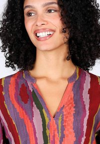 Bunte gestreifte Bluse in Lila, Rot und Grün. Sie verfügt über einen V-Ausschnitt und einen strukturierten Stoff mit einer lockeren, entspannten Passform.