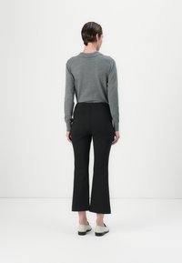 Top grigio a maniche lunghe e pantaloni neri a zampa d'elefante, che mostrano una silhouette aderente. Il modello indossa scarpe basse di colore chiaro. Design minimalista.