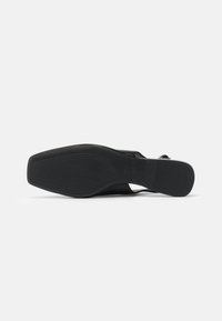 Semelle de chaussure noire, design plat avec des rainures horizontales, fabriquée en caoutchouc. Forme arrondie avec une légère courbure, sans marque ni embellissements visibles.