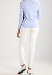 Maglione azzurro chiaro a maniche lunghe abbinato a jeans bianchi aderenti e sneakers bianche. Il maglione presenta una texture liscia e un design minimalista.