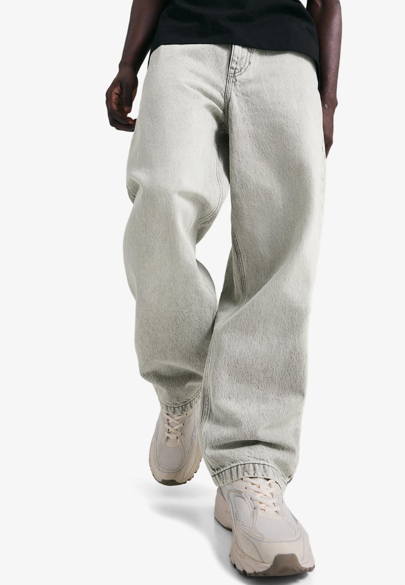 Világosszürke farmernadrág, laza szabással és szűkített bokarészekkel, finom textúrával és oldalzsebekkel, bézs sportcipővel párosítva.