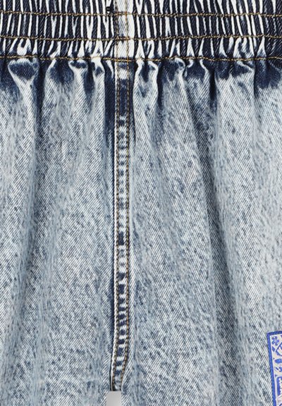 Tissu en denim bleu clair à effet délavé avec une taille élastique froncée et des coutures orange contrastantes.