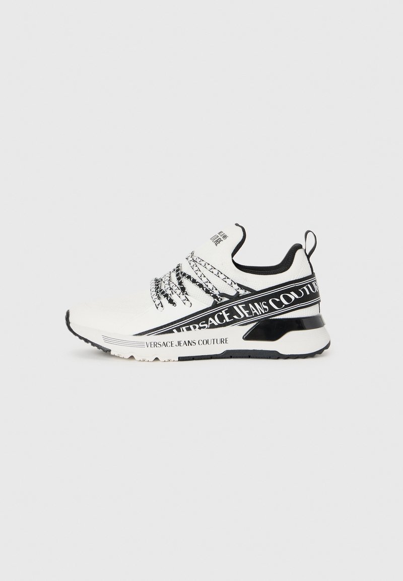 Białe sportowe sneakersy z czarnymi akcentami, z teksturowanym cholewką, wzorzystymi sznurówkami i wyraźnym logo na boku.
