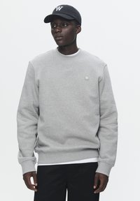 Gray sweatshirt with ribbed cuffs and hem, featuring a small circular logo. Paired with a black cap displaying a white logo. Black pants.