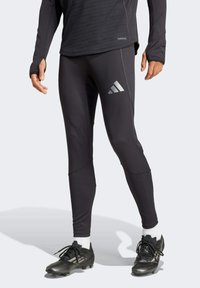 Schwarze Sportleggings mit einer enganliegenden Passform und dezenten silbernen Akzenten. Gezeigt werden auch schwarze Sportschuhe und weiße Knöchelsocken.