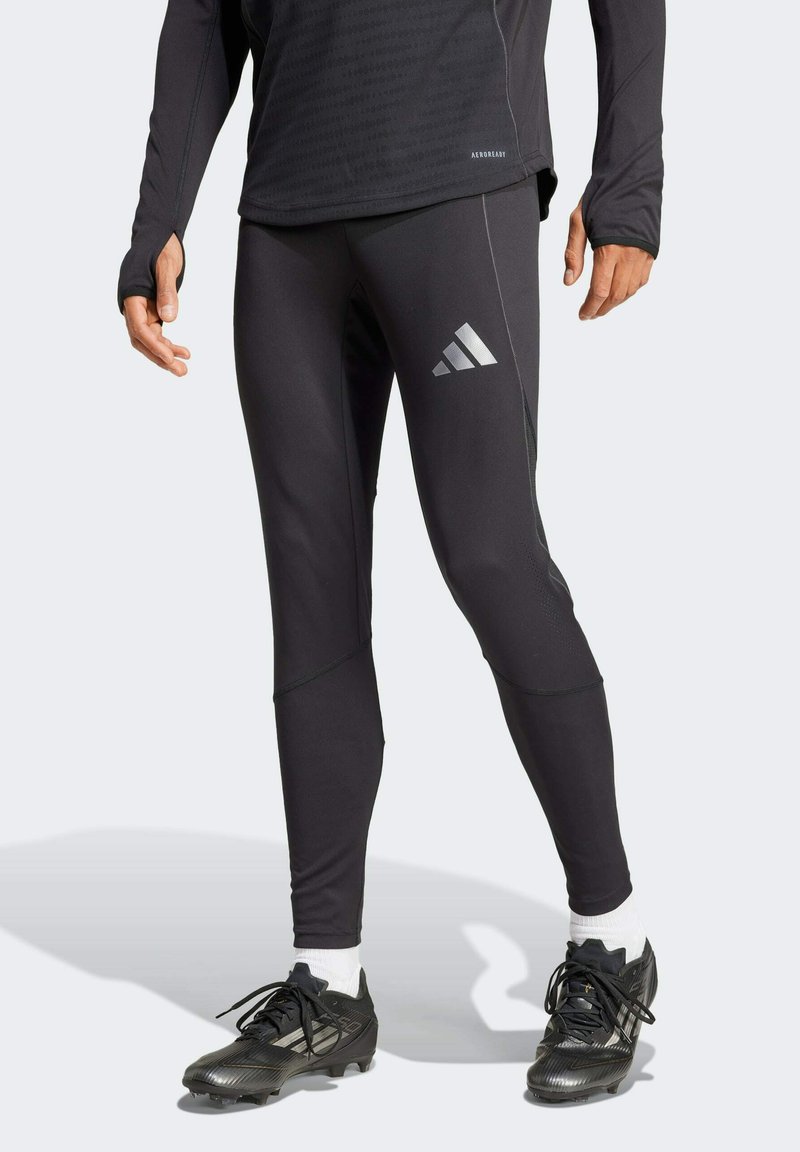 Schwarze Sportleggings mit einer enganliegenden Passform und dezenten silbernen Akzenten. Gezeigt werden auch schwarze Sportschuhe und weiße Knöchelsocken.