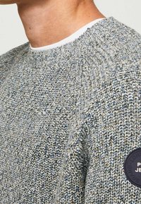 Gestrickter Pullover in Grautönen und Blau mit strukturiertem Finish. Merkmale einen runden Halsausschnitt und ein rundes Logopatch am Ärmel.