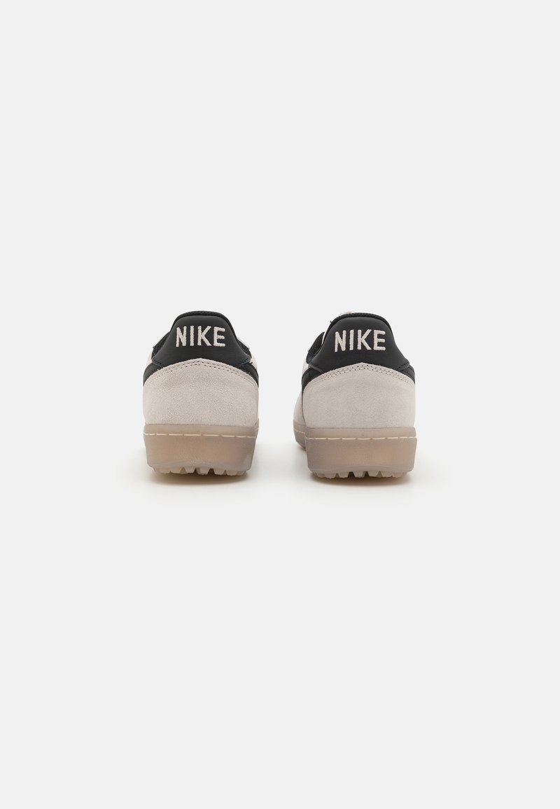 Sneakers Nike con una combinazione di colori nero e beige, in materiale scamosciato, forma arrotondata e suola in gomma. Logo "NIKE" ben visibile sul tallone.
