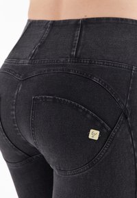 Musta korkeavyötäröinen denim leggings, joissa on sileä pinta, kaarevat saumat ja pieni etiketti takataskussa.