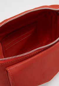 Cartera de cuero rojo con cremallera, con varios compartimentos para tarjetas y una superficie lisa y texturizada. El interior presenta un forro liso y el logo de la marca.