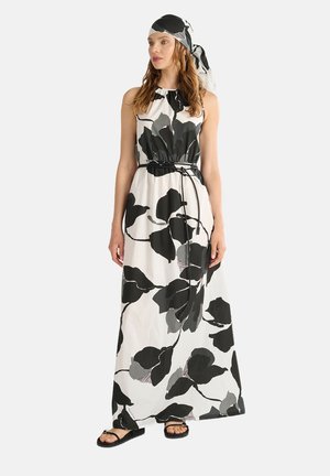 Maxikleid in Weiß mit großen schwarzen und grauen Blattmustern. Mit hohem Kragen, elastischem Bund und passendem Kopftuch. Flache Sandalen.