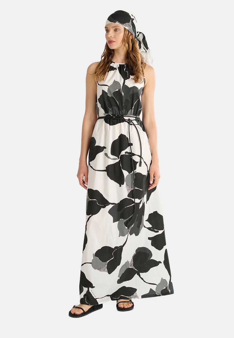 Abito maxi bianco con grandi motivi di foglie nere e grigie. Presenta un colletto alto, vita elastica e un foulard abbinato. Sandali piatti.