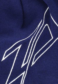 Sininen neulottu kangas, jossa on sileä pinta, valkoisilla brodeeratuilla vinoilla viivoilla ja rohkealla graafisella elementillä.