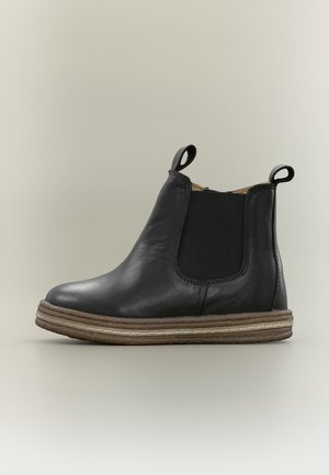 Bottine Chelsea en cuir noir avec semelle en caoutchouc marron et panneaux latéraux élastiques noirs, avec languettes à l'avant et à l'arrière.