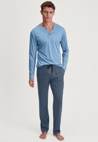 Lichtblauw langslavend henley shirt met drie knopen, gecombineerd met marineblauwe pyjamabroek met een geometrisch patroon.