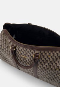 Brown patterned duffle bag with gold accents, featuring a zip closure and leather handles. Interior is black fabric with a side pocket.