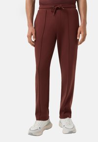 Bordeaux sportieve broek van een zachte stof, met een trekkoord in de taille, zijsplitten en gecombineerd met witte sneakers.