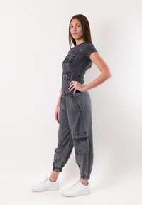 Camiseta gráfica gris de manga corta con texto en múltiples colores, acompañada de pantalones jogger grises sueltos con puños elásticos y bolsillos laterales.