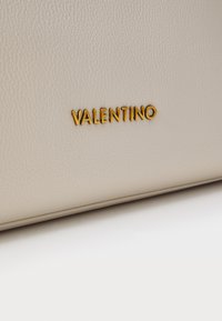 Bežna usnjena torba z teksturirano površino in zlate barve "VALENTINO" logotip, ki je izpostavljen. Preprost, eleganten dizajn.