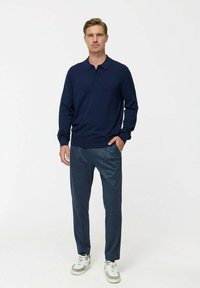 Polo cu mânecă lungă de culoare bleumarin, cu guler, asortat cu pantaloni texturați de un albastru închis și adidași albi cu accente gri.