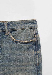 Džínové kalhoty v bledě modré barvě, s designem pěti kapes, kovovými doplňky z mosazi a význačnými variacemi struktury.