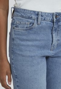 Jeans de denim azul claro con cintura alta, que presentan un diseño clásico de cinco bolsillos y costura visible. La textura parece suave y lisa.