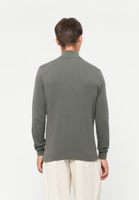 Grå strikkegenser med kragehals, lange ermer, ribbede mansjetter og nederkant. Glatt tekstur, tettsittende design og minimal detaljering.