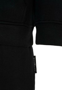 Czarna bawełniana bluza z ściągaczami przy mankietach i dolnym brzegu, z tagiem z boku. Gładka textura o prostym designie.