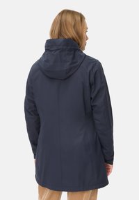 Veste imperméable bleu marine avec capuche, dotée d'une texture lisse et d'une coupe allongée, détaillée avec une couture centrale au dos et des poignets élastiques.