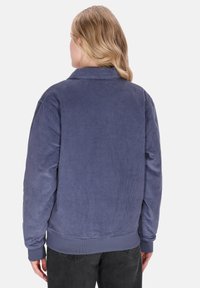 Granatowa kurtka sztruksowa z kołnierzykiem i prążkowaną fakturą, zestawiona z czarnymi spodniami. Krój jest luźny z długimi rękawami.