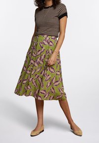 Gonna verde plissée con motivo a foglie viola, abbinata a una maglietta a maniche corte bianco e nera con un motivo e ballerine intrecciate marrone chiaro.